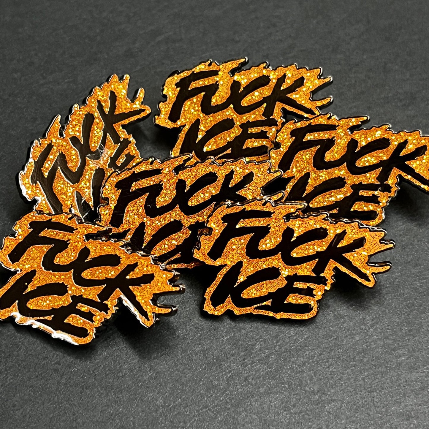 Multiple orange and black 'F*ck Ice' pins on a dark background